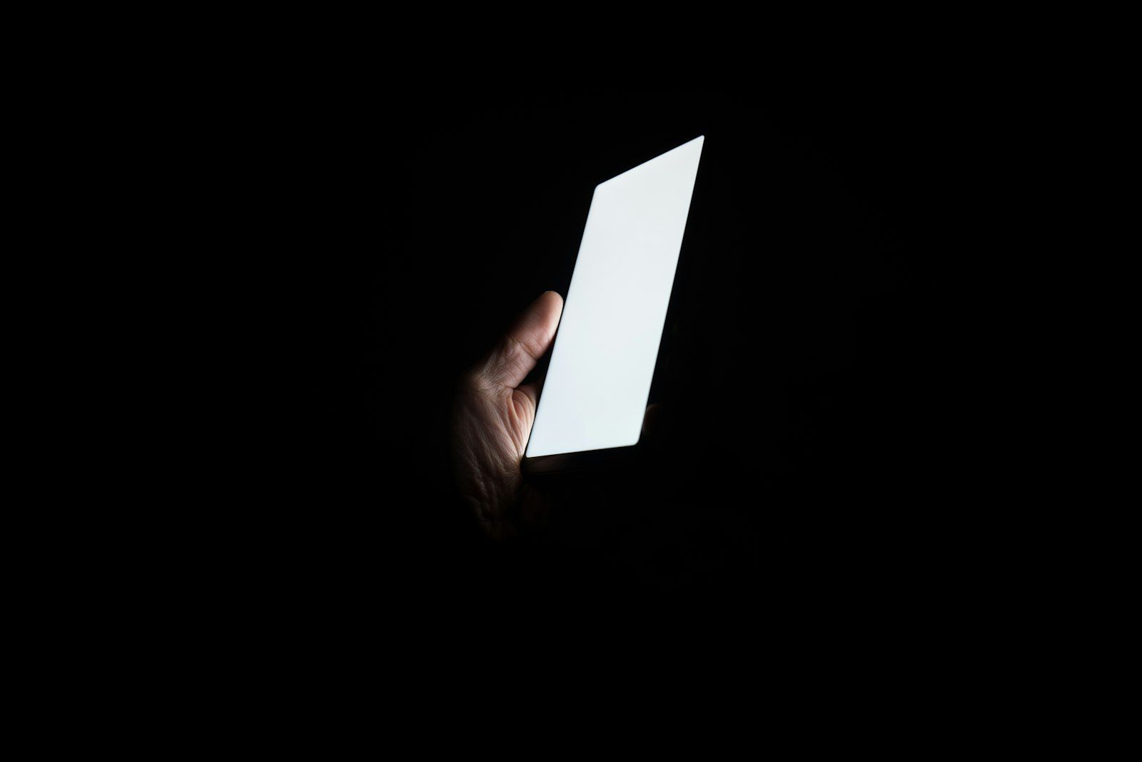 A hand holding a smartphone, its screen glowing in the dark