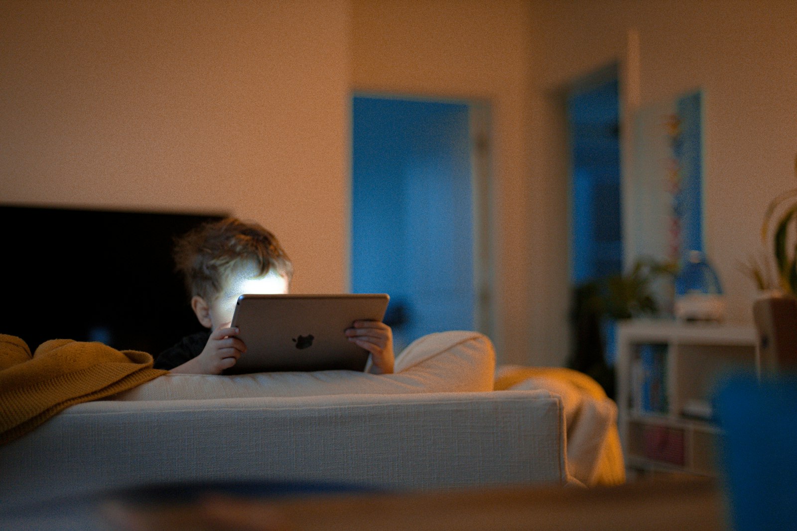 A young child on a couch in a dim room, face lit by the glow of a tablet
