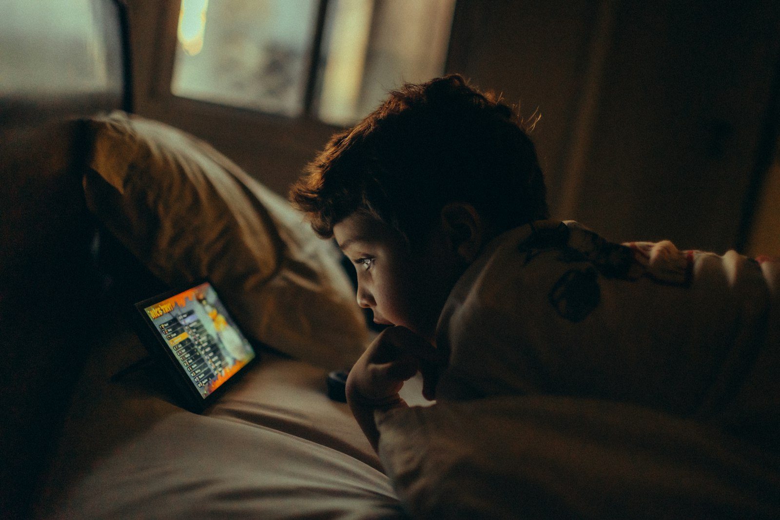 A young boy watching a tablet in bed at night