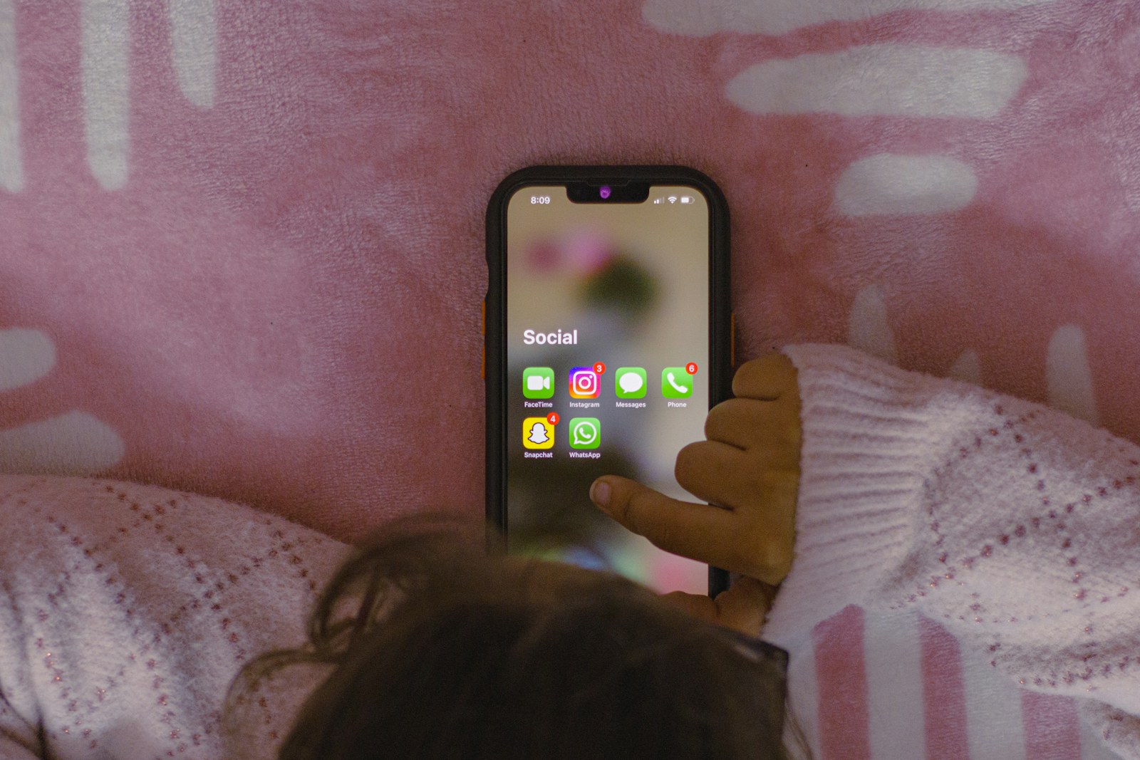 A child reaching for a smartphone showing a Social folder with Instagram, Snapchat, WhatsApp, and Messages