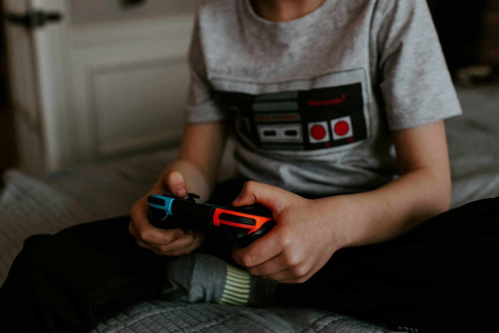 A child's hands holding a game controller while sitting on a bed