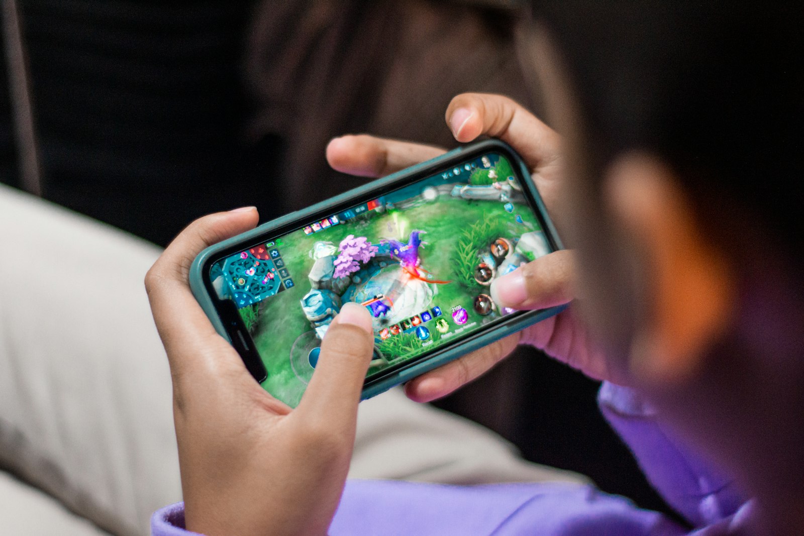 A child&rsquo;s hands holding a phone sideways, mid-game in a colourful mobile battle game