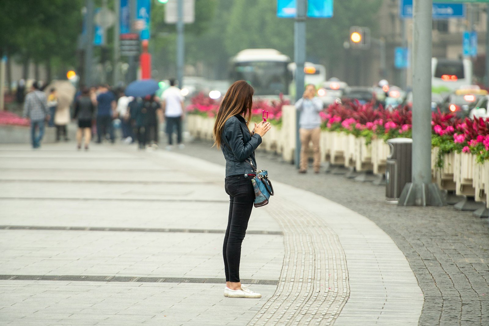A young woman standing independently on a city sidewalk, using her phone
