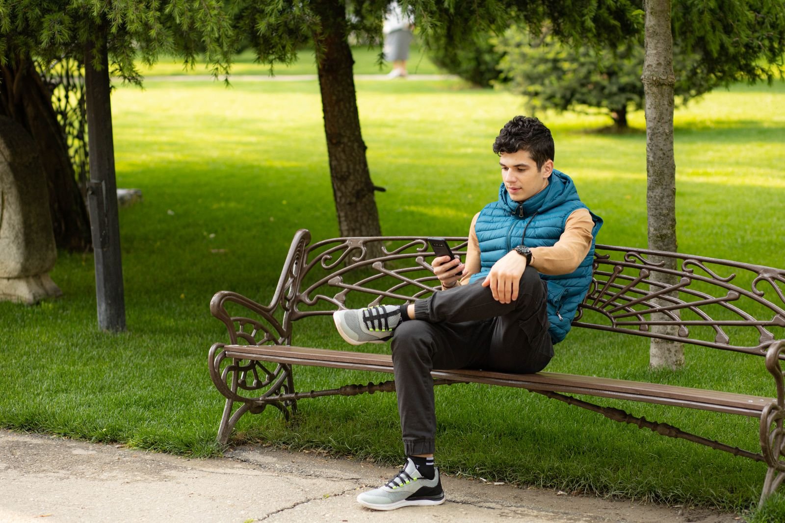 A boy sitting on a park bench looking at his phone