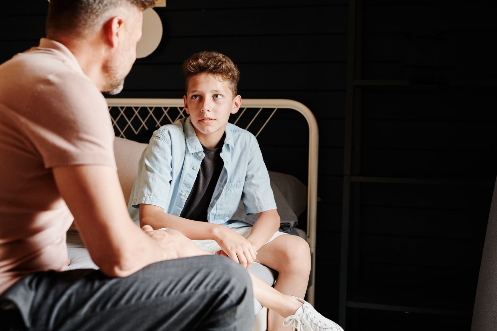 A father and his son sitting on a bed having a calm, quiet conversation