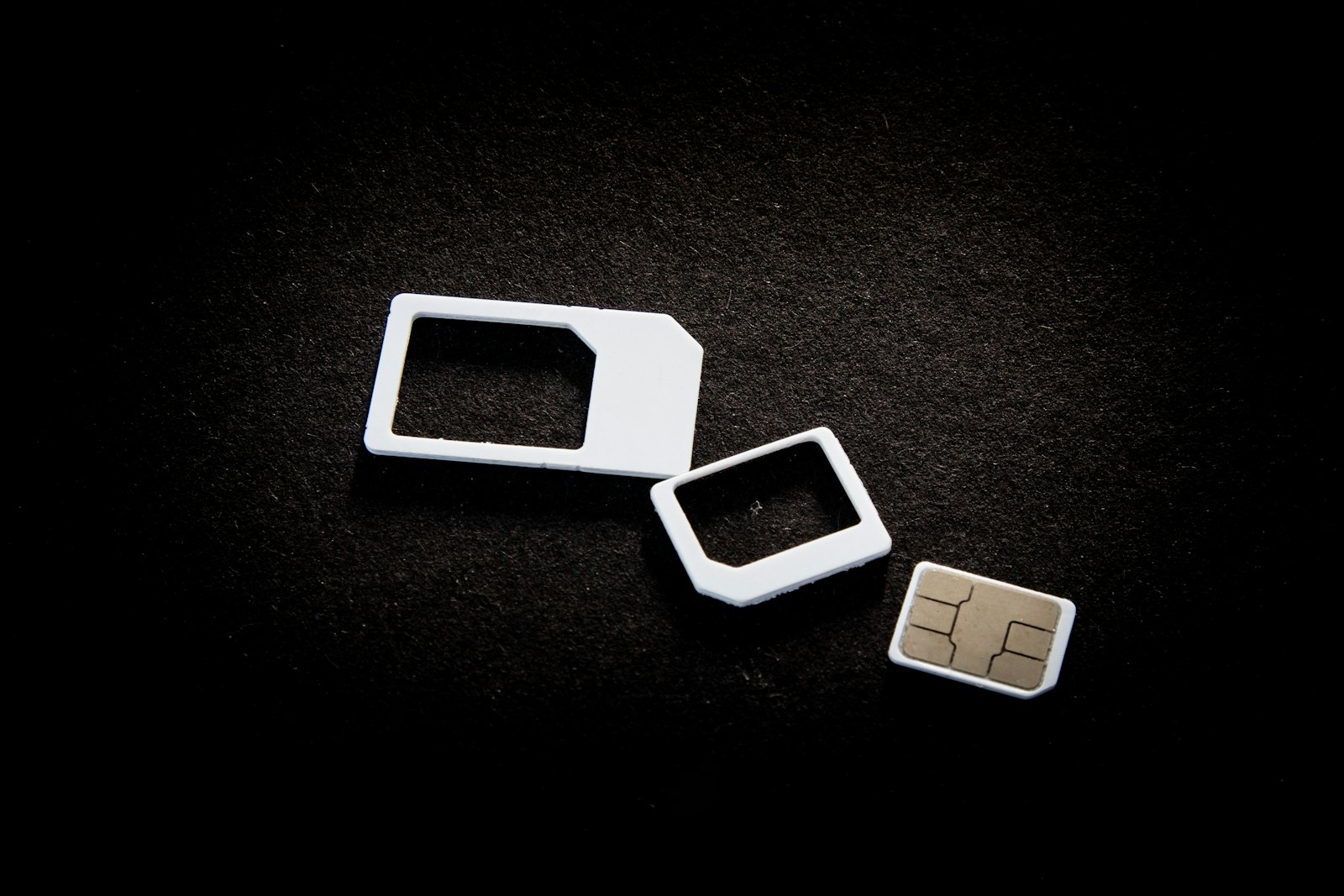 Three SIM card sizes, a full-size adapter, a micro adapter and a nano SIM, on a dark background