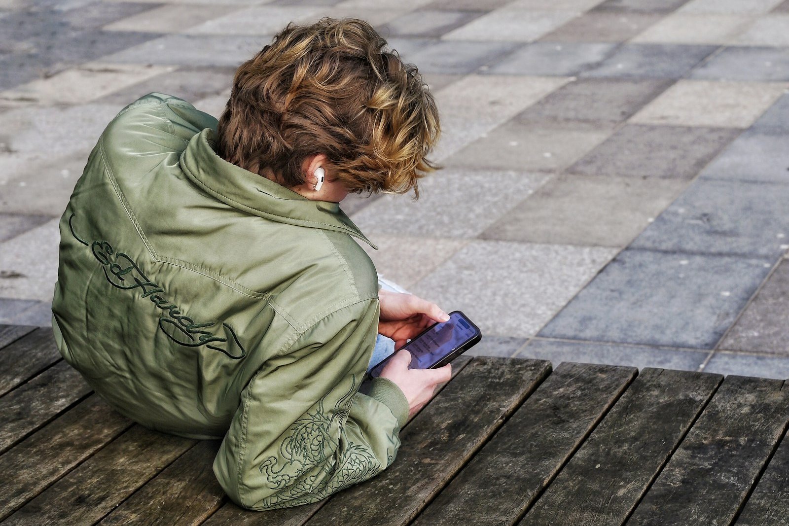 A young person seen from behind, absorbed in their phone