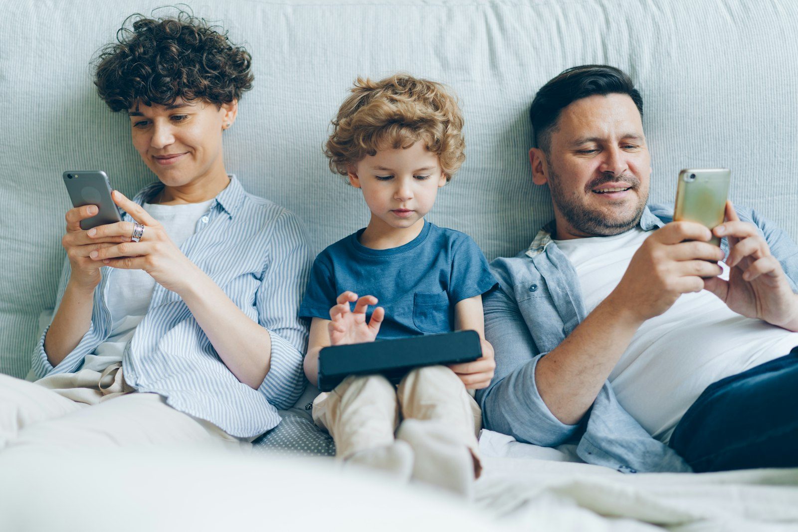 A family on a couch, each looking at their own phone — the everyday moment these three separate controls are actually managing